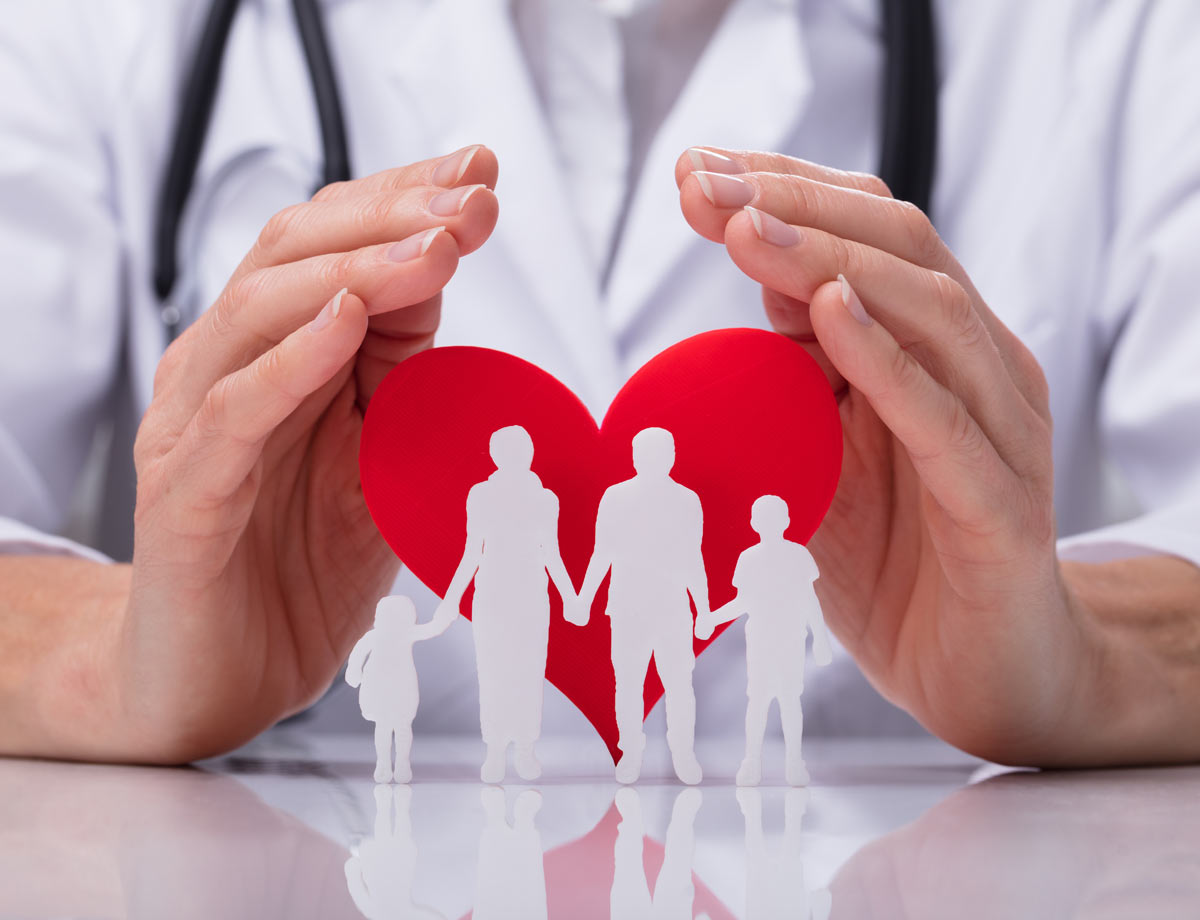 truncated image two hands encompassing a paper cutout of a red heart with paper people holding hands