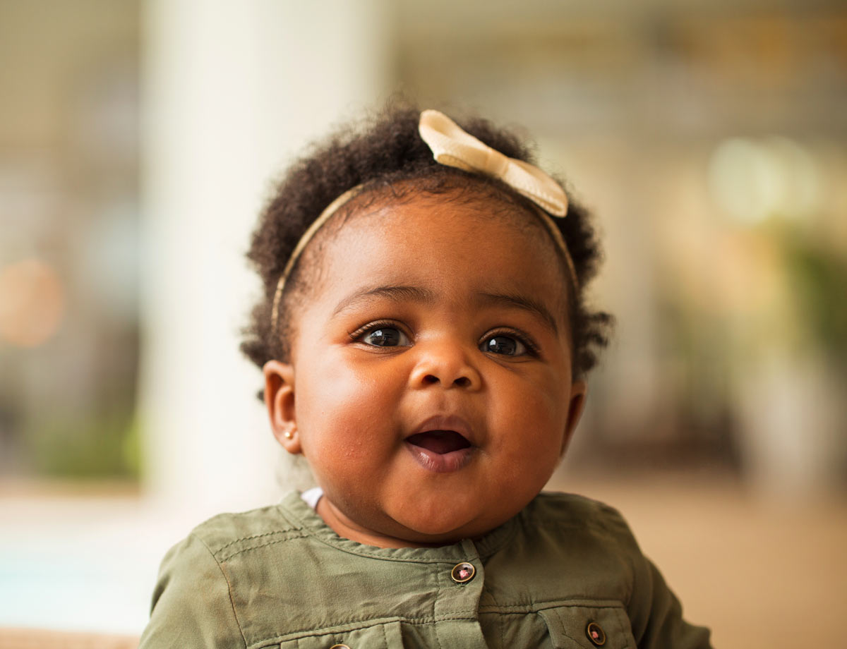 an image of a chubby faced infant sitting on the floor smiling